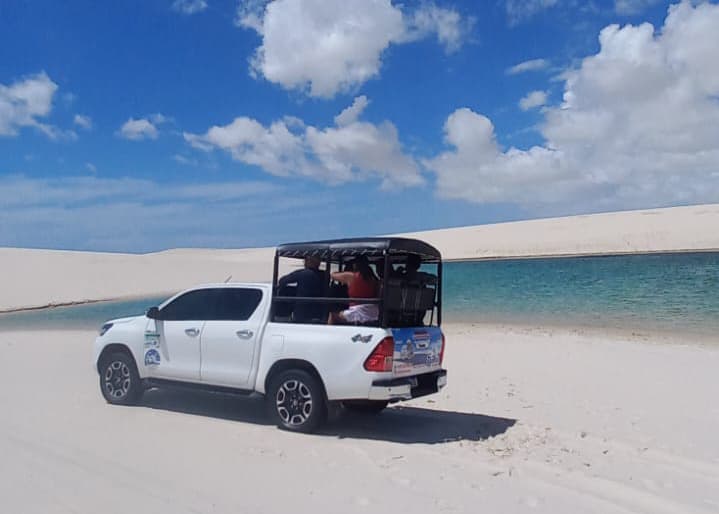 Hilux 4x4 com turistas na caçamba cruzando lagoa no Circuito Betânia dos Lençóis Maranhenses