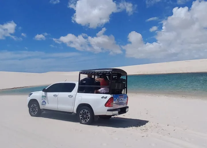Hilux 4x4 com turistas na caçamba cruzando lagoa no Circuito Betânia dos Lençóis Maranhenses