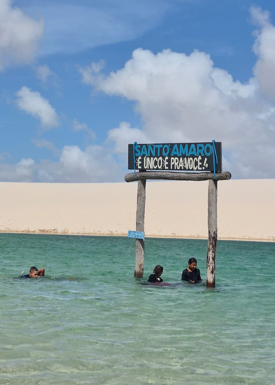 Placa Santo Amaro É Único É Pra Você com crianças banhando na lagoa dos Lençóis Maranhenses