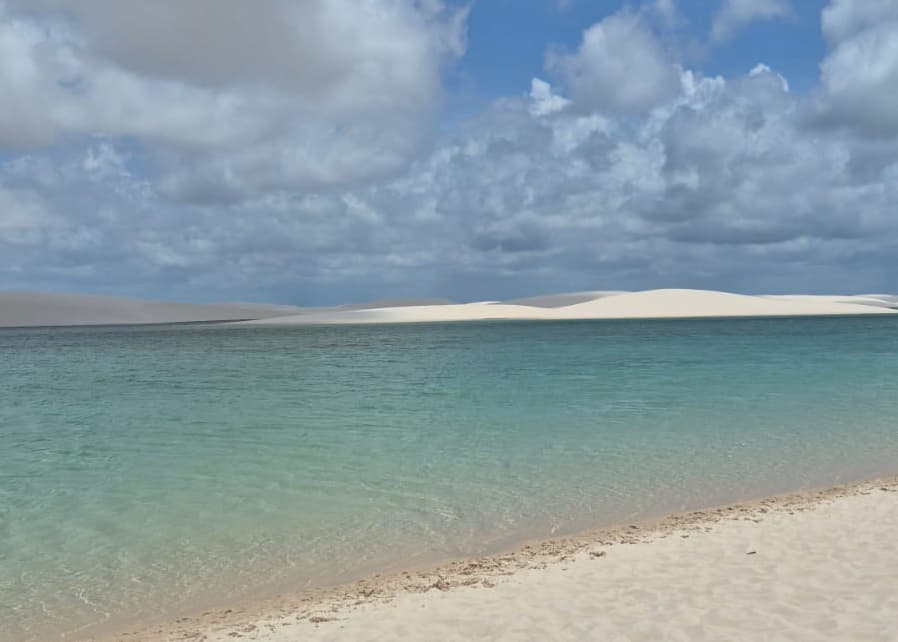 Lagoa turquesa ampla com dunas brancas ao fundo nos Lençóis Maranhenses