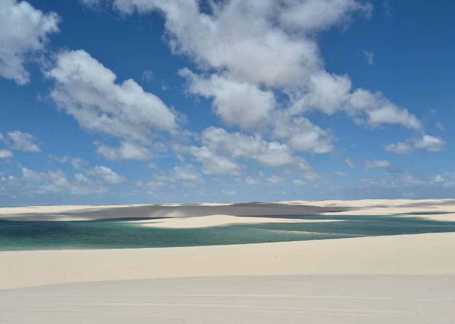 Lagoa turquesa com margem de areia branca e dunas nos Lençóis Maranhenses